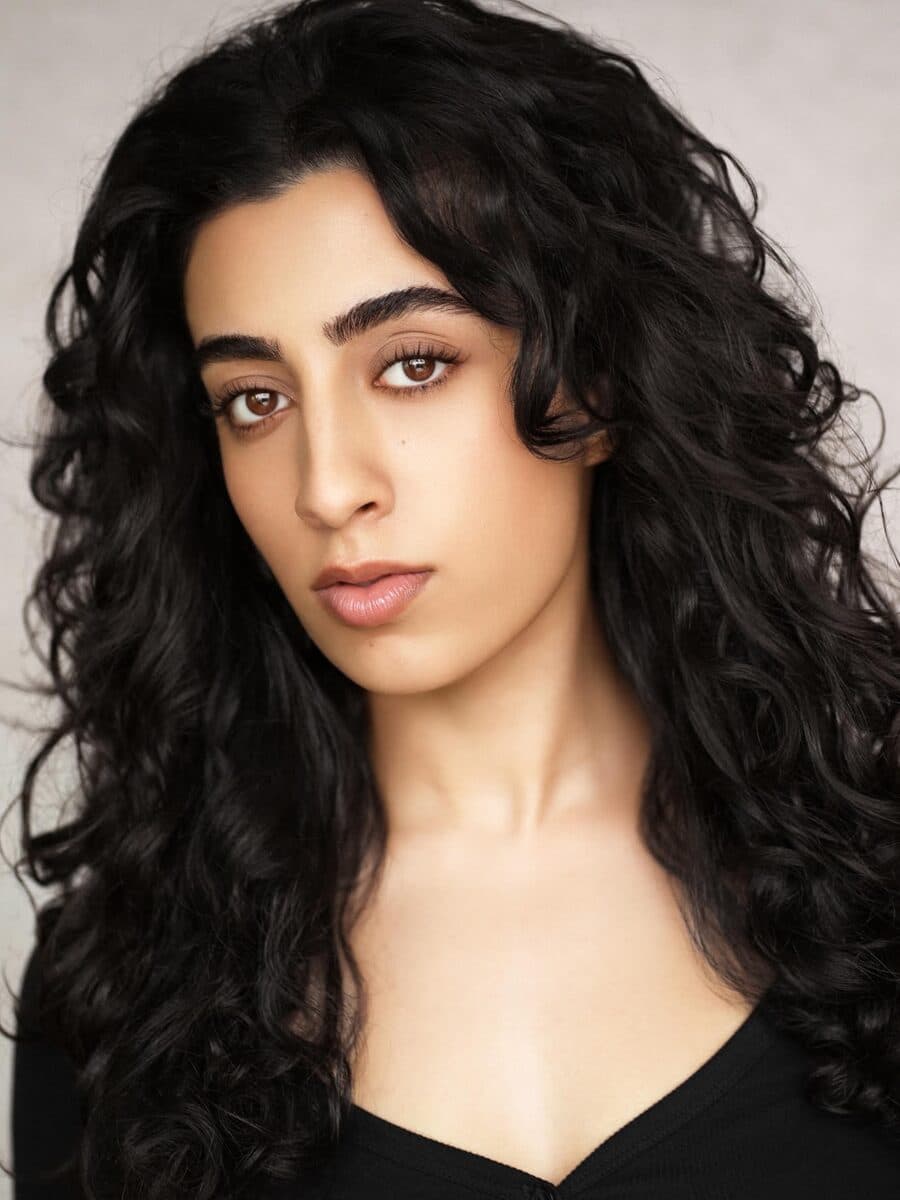 Long dark curly hair and a black top, on a light grey ground.