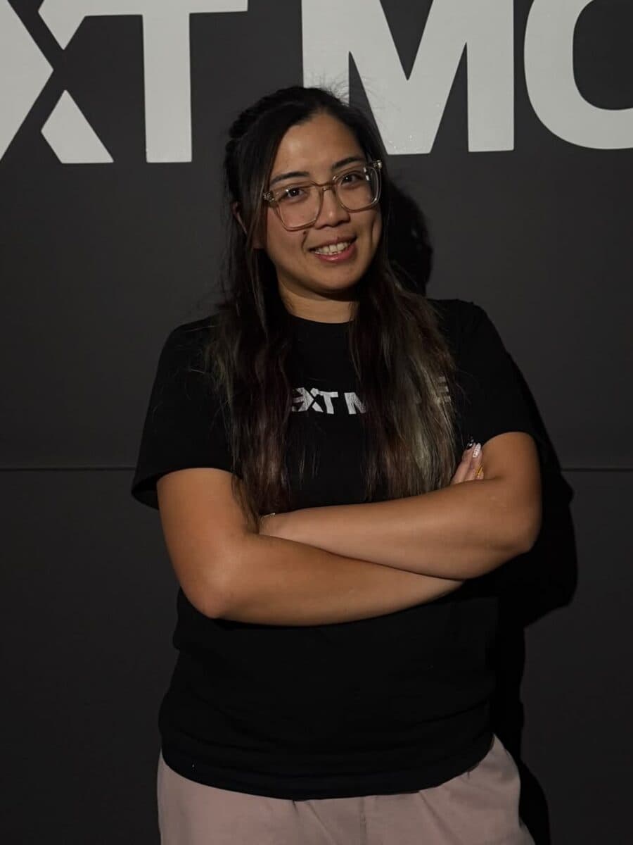 In glasses and a black tee, arms crossed, in front of the studio's logo wall.