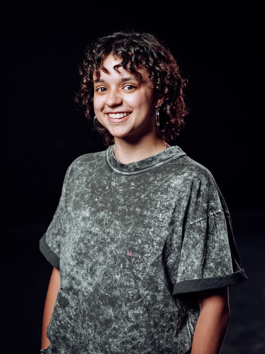Smiles in a grey tee, on a black ground.
