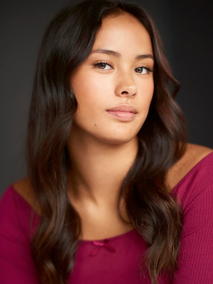 Long dark hair and a magenta top, on a dark grey ground.