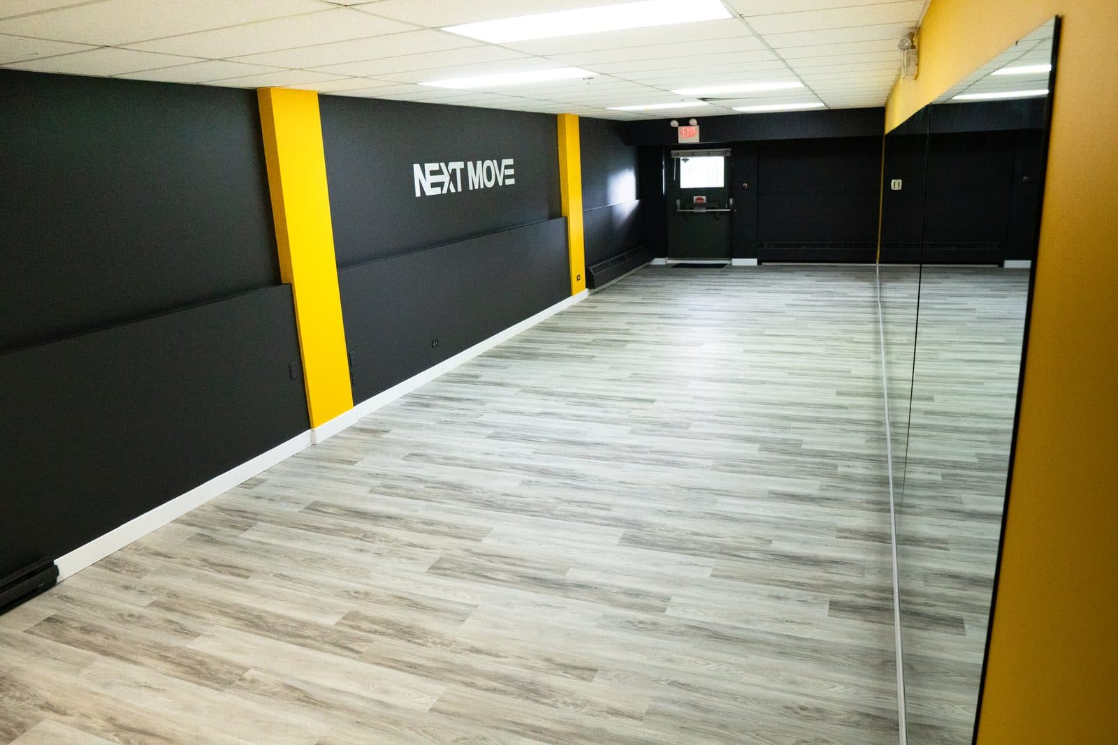 The Platform from the corner: black walls with the Next Move logo between yellow pillars, a grey wood floor and a mirror on the right.