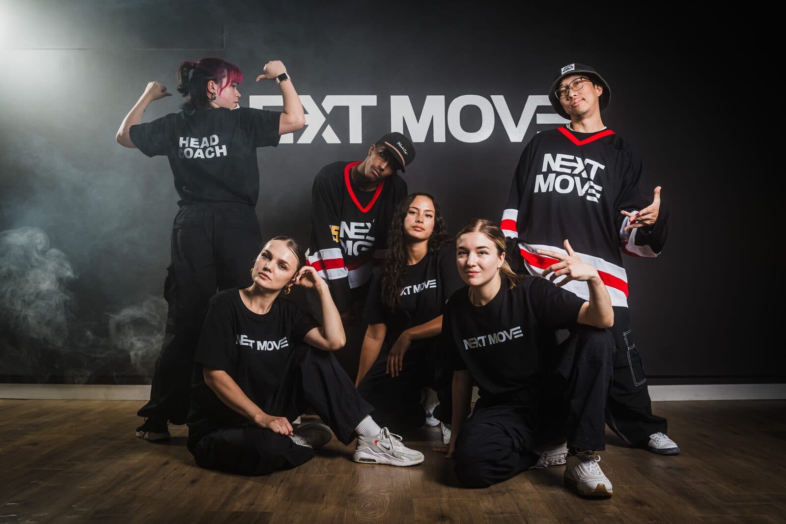 Six mentors pose together in front of the studio's logo wall, three standing and three low on the floor.