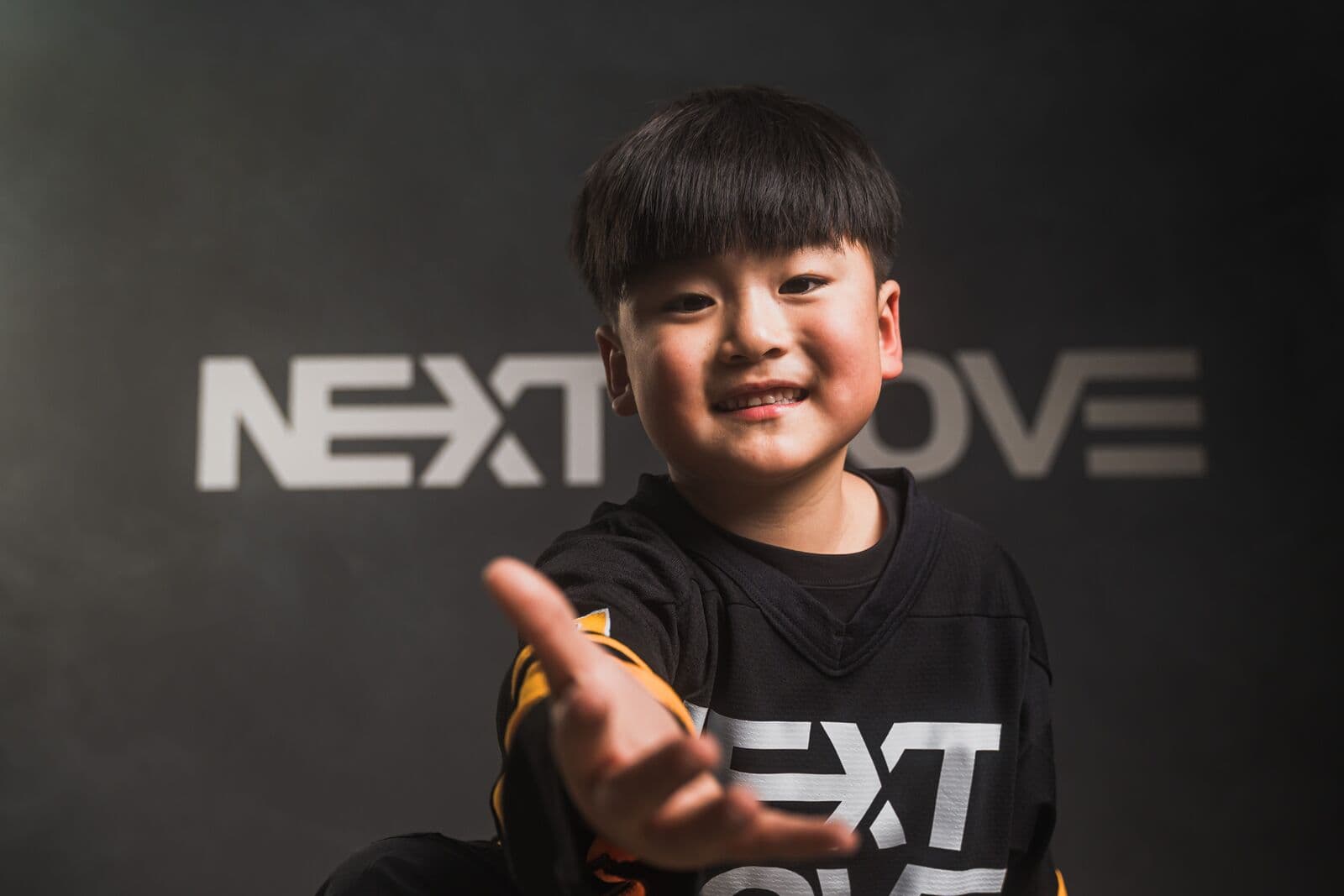 A smiling young dancer in a Next Move jersey reaches one hand toward the camera.